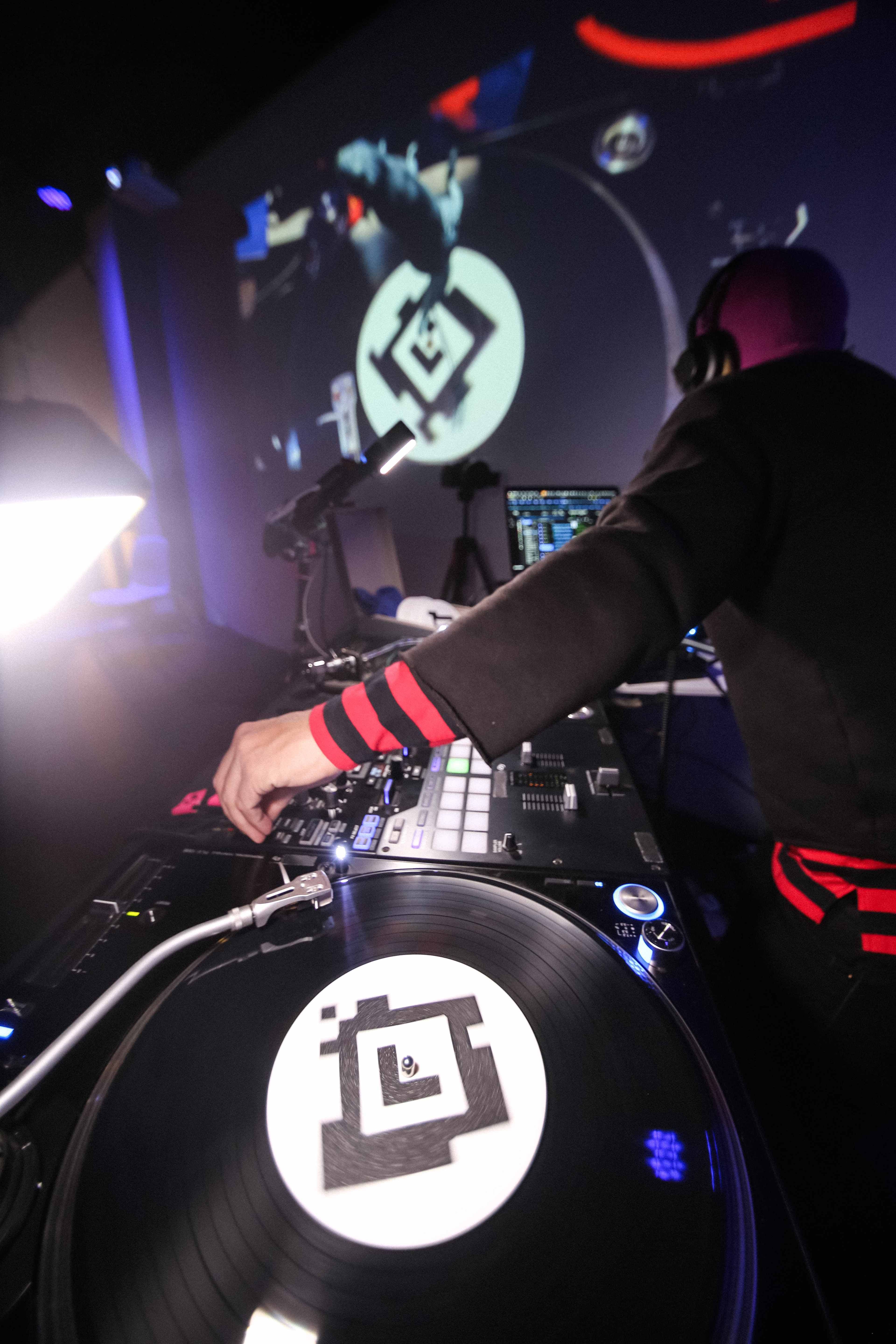 Rob Ray standing behind the DJ booth facing his laptop. A vinyl record with AR target on the label.