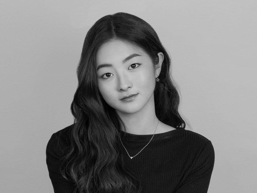 A black and white photo of an Asian woman wearing a plain black long t-shirt and necklace.